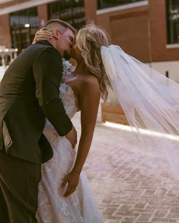 A couple kissing beneath her veil on a brick street